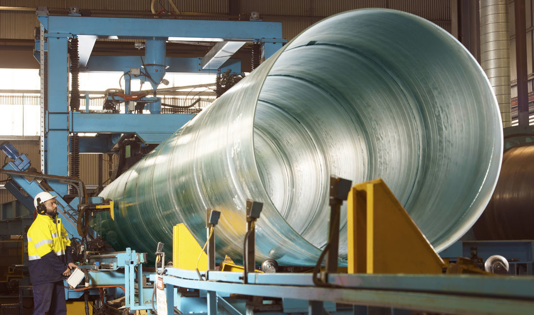 A worker at the controls of the mill line beside a large-diameter spiral-welded steel pipe